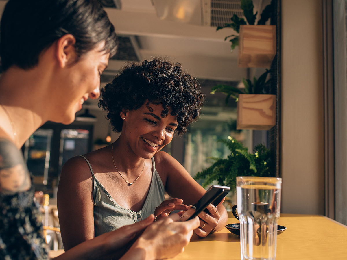 Two women sitting at a table, focused on their phones while enjoying each other's company.