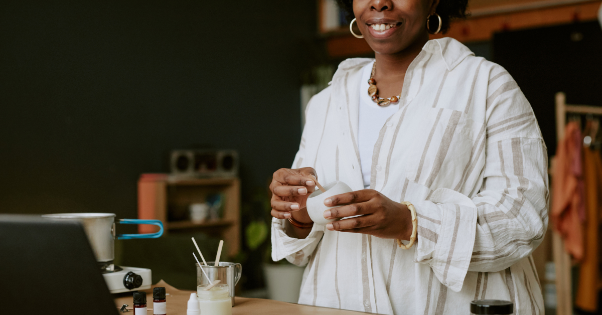  A woman is smiling as she works on making a candle. 