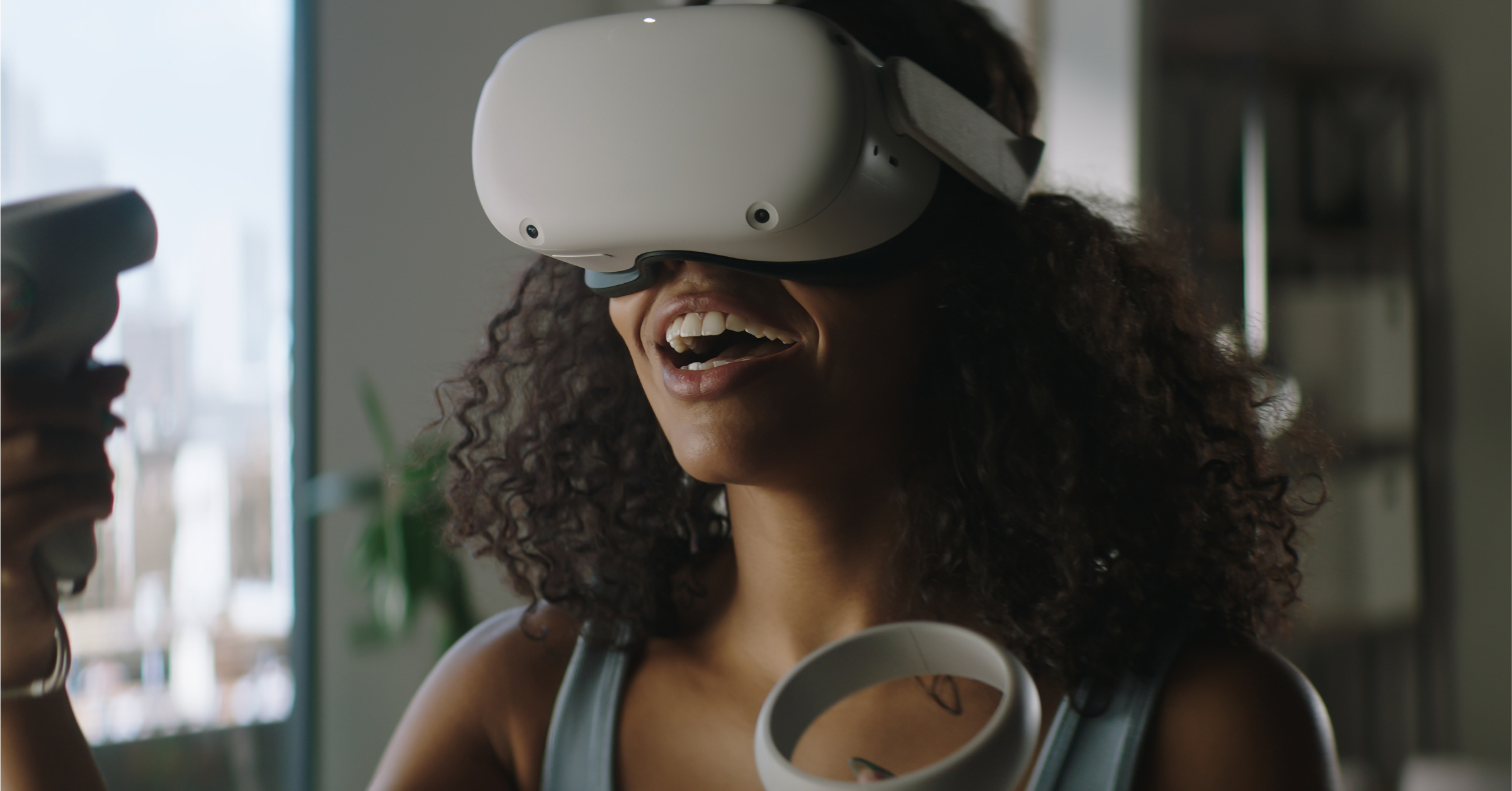 A woman with curly hair smiling while wearing a white virtual reality headset and holding controllers, immersed in a VR experience.